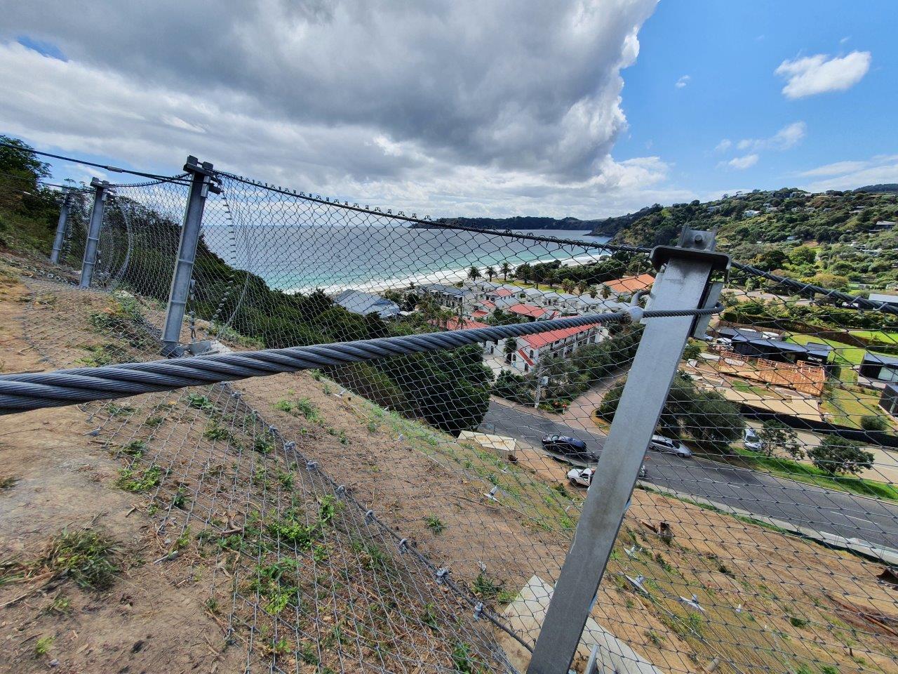 Rock fall catch fence on a steep slope above a coastal suburb