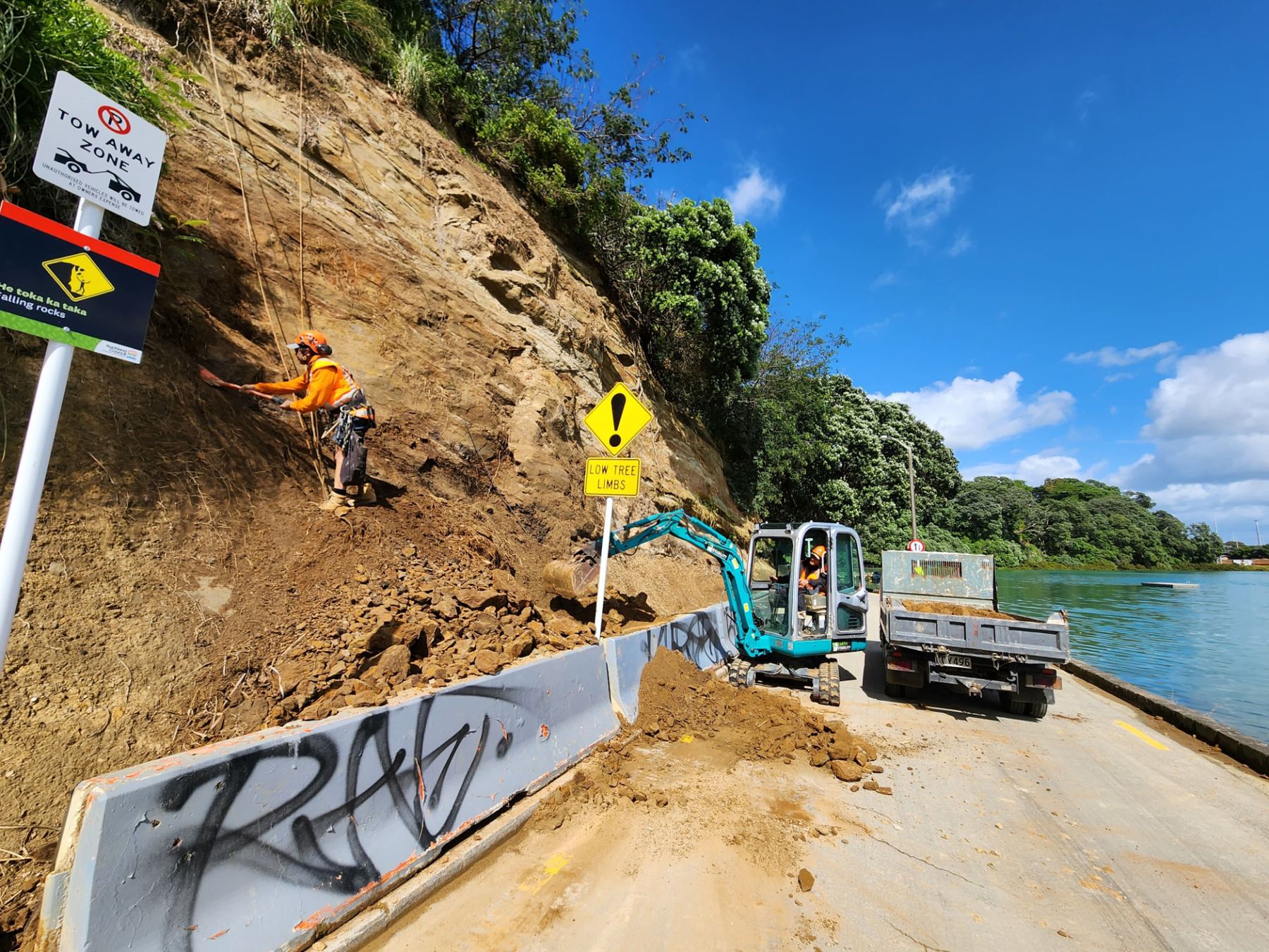 Rope access technician clearing loose material from a slip face above a coastal road
