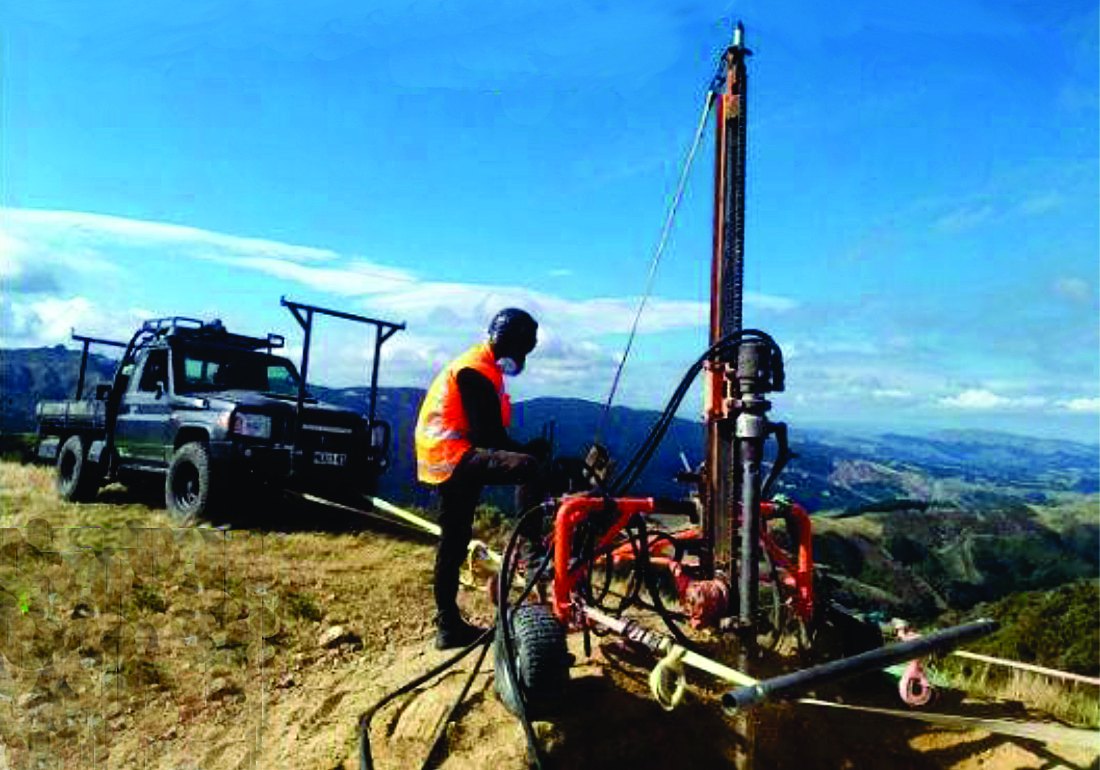 Earth Stability crew member operating a portable micropile drill rig on a remote hilltop, with a 4x4 utility truck behind