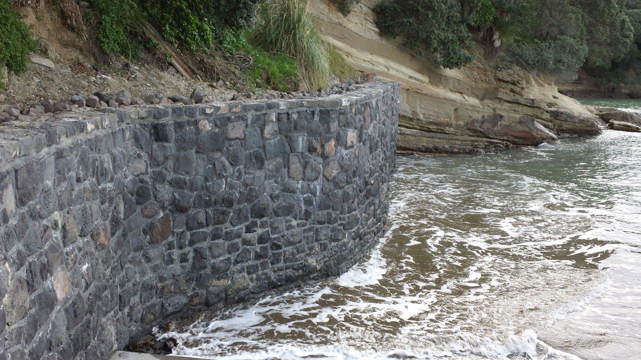 Curved basalt stone seawall standing against the tide at the beach