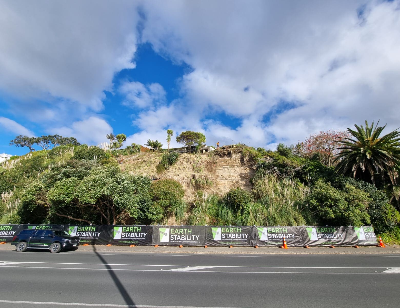 Long run of branded safety scrim along a main road below a vegetated slope
