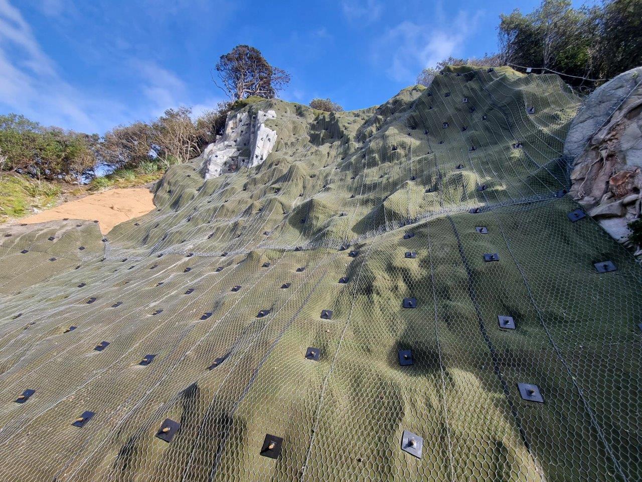 Anchored mesh and erosion matting protecting a reinstated coastal slope