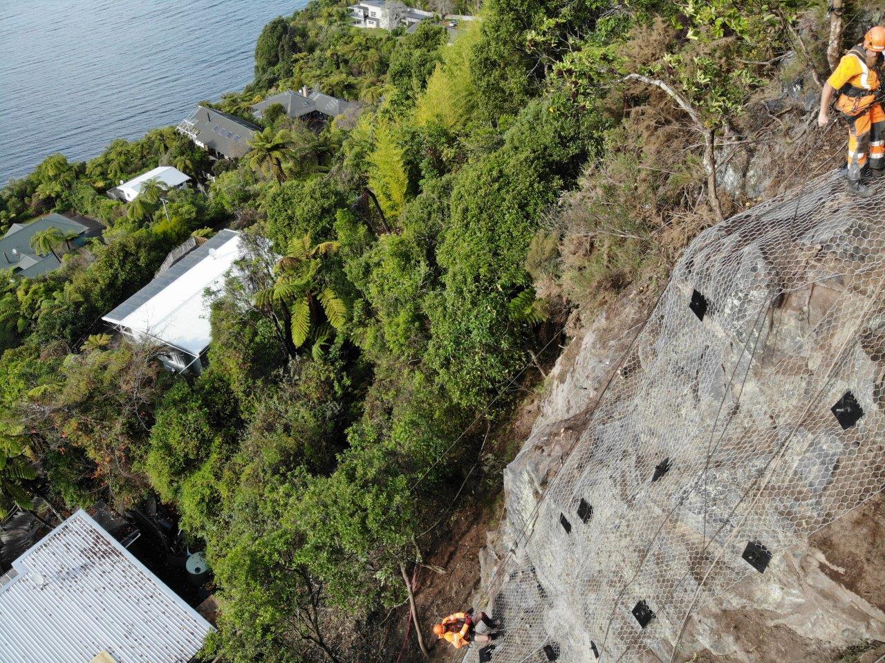 Aerial view of anchored mesh being installed on a bluff above lakeside houses